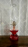 Full view of antique oil lamp with ribbed clear glass base filled with red oil and tall glass chimney