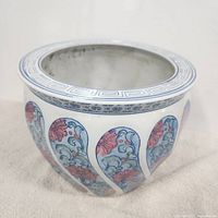 Front side view of porcelain planter showing pink and blue-green floral scroll motifs with geometric border on rim.