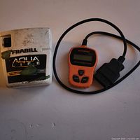 Photo showing the Autophix OM121 OBD2 car diagnostic tool with cable and the Frabill Aqua Life aeration system side by side on a surface.