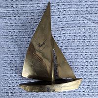 Top view of brass sailboat decoration displaying its single large sail and secondary smaller sail with reflective brass material.