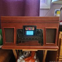 Front view of Crossley audio system showing wooden casing, speakers, control panel with knobs and buttons, and display screen.