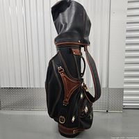 Side profile of vintage black and brown leather golf bag showing multiple zippered compartments and leather shoulder strap