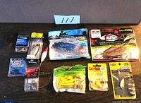 Lot of 10 fishing baits displayed on table including packaged soft baits, jig heads, crankbaits, spinnerbaits, and assorted fishing lures.