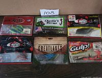 Six fishing bait packages shown on wooden surface with identifier card '108'.