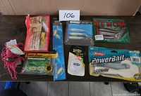 Lot of 8 fishing baits arranged on a table, including spinnerbaits, soft plastic worms, trusty lures in original packaging.