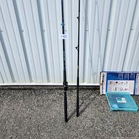 Two black fishing rods standing upright against a metal wall, showing full length