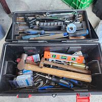 Top view of open Jobmate black plastic toolbox, showing various hammer types, screwdrivers, spirit level, wrench, file, tape and other hand tools inside.