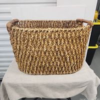 Front view of large rectangular handwoven wicker basket with braided handles.