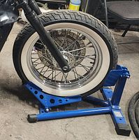 Front wheel of motorcycle secured in blue metal wheel stand on concrete floor.