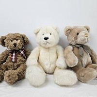 Three stuffed teddy bears in brown, cream and beige colors sitting against a white background.