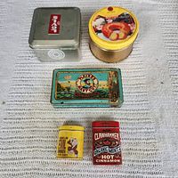 Top-down photo of six vintage tins arranged on fabric surface showing labels and designs