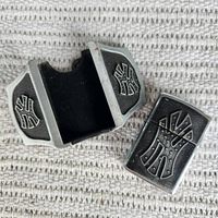 Metal belt buckle open with removable Zippo lighter beside it on a textured textile background. Both have Yankee logo designs in black and silver.