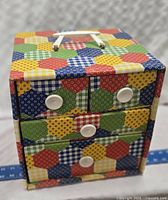 Colorful vintage sewing box showing front with three drawers and white knobs