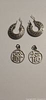 Silver hoop earrings with Greek key pattern and hook backs shown on white background.