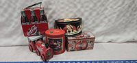 Full view of four Coca-Cola collectible tins including a 6 pack lunchbox shaped tin and three decorative tins with vintage style artwork.