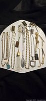 Photo showing nine assorted costume jewelry necklaces on a white plate with pendants including stones, tassels, teardrops, and geometric shapes in gold and silver tones.