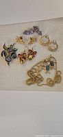 Photo showing all jewelry items included: a handmade enamel pin, various earrings, and a gold-tone necklace with pendant