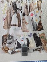 Cat-themed fabric shower curtain with images of various cats and butterflies, hanging with curtain hooks and soap dispenser in front.