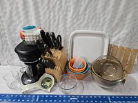 Photo showing the Mr. Coffee maker, wooden knife block with knives, Pyrex bowls, cutting board, silicone measuring cups, and other assorted kitchenware items on a white surface