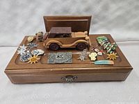 Wooden vintage men's jewelry box with pull-out drawer open and closed, displaying a wooden miniature car on top, surrounded by various vintage pins, brooches, earrings, and a small teddy bear figurine.
