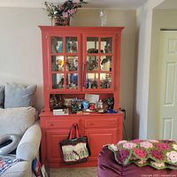 Two-piece red wooden hutch against wall, upper cabinet has glass doors with multiple panes, lower cabinet with two drawers and two doors. No items included inside.
