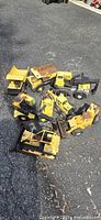 Seven vintage metal Tonka construction trucks arranged on asphalt. Various types including dump trucks, bulldozers, and loaders in yellow and black color.