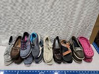 Photo showing nine pairs of used women's shoes size 7 in various styles and colors lined up in a row