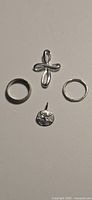 Four small silver jewelry items on white background: two rings and two pendants, one ring marked 925 with size noted, one cross pendant, one round floral pendant.