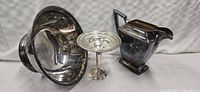 Set of three silver serving pieces arranged together: large bowl, pedestal compote, and pitcher.