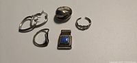 Lot overview of six silver jewelry pieces including five rings and one pendant.