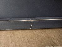 Close-up photo of the crack on the black frame of the wall decor showing damage to the wood and paint.