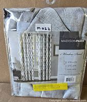 Curtain panel still in plastic packaging showing label with sizing options and product image.