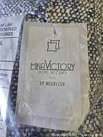 Close-up of the Mina Victory Home Accents tag by Nourison attached to the pillow showing brand and confirming authenticity.