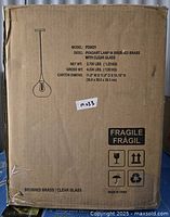 Cardboard box packaging with printed model information: Model PD0621, description pendant lamp in brushed brass with clear glass, weight and dimensions, fragile symbols, and label M033.
