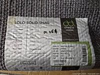Close-up of Unique Loom rug label showing product specifications including quality Solo Solid Shag, design 00063A, graphite gray color, size 2'x3'.