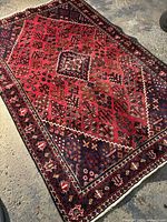 Full view of hand-knotted rug on concrete floor showing red field with geometric motifs and navy border