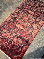 Full view of the Persian rug laid flat showing its geometric and floral motifs with dominant black and burgundy natural colors.