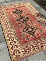 Full view of the Persian rug laid on pavement showing overall geometric pattern, colors, and condition.