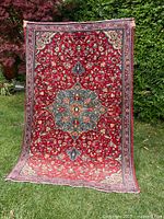 Full view of red Persian rug leaning against greenery
