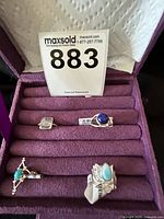 Photo showing four sterling silver rings with different gemstones in a purple velvet ring box.