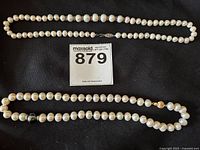 Both pearl necklaces laid flat on black background showing overall strands