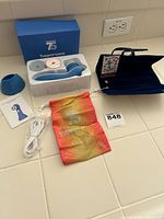 Overall lot view showing the blue Brighton jewelry pouch with anchor pattern alongside Tupperware 75th anniversary facial cleansing kit components on white countertop.