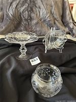 Photo showing the three clear glass Cambridge Portia pieces on a black cloth backdrop with floral etching visible, including the stemmed comport, candy dish with keyhole handle, and ball vase.