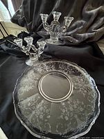 Photo of large etched glass torte plate with scalloped edge and two keyhole style Cambridge Portia candle sticks behind it on black cloth