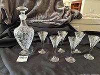 Photo showing the etched glass sherry decanter with stopper and six matching glasses laid out on a dark cloth.