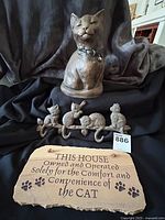 Carved stone cat statue, cast iron cat hook, and carved stone plaque arranged together on black fabric background