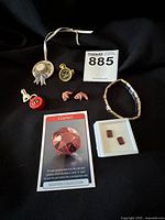Photo of assorted costume jewelry on black fabric including Longaberger hat tie-on, watch pin, lock and key charm, carved elephants, garnet earrings on card, and bracelet.