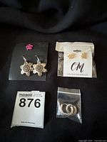 All three pairs of earrings shown: silver snowflake dangles, gold cat studs in package labeled Charming & Main, and small silver filigree hoops in small plastic bag.