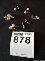 Shows 5 pairs of stud earrings and one pearl ear cuff on a black background with lot number card 878