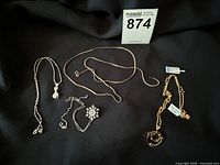 Four necklaces laid out on black fabric: three sterling silver with distinct pendants (cat with opal, snowflake with clear stones), one gold over silver chain with gemstone pendant.